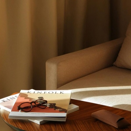 A table with a book and glasses on it next to a couch in the sunlight.